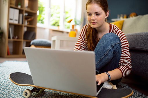 Redhead Caucasian teenage girl, using a laptop, while sitting on the floor in the living room