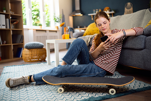 Redhead Caucasian teenage girl, using mobile phone, while sitting on the floor in the living room