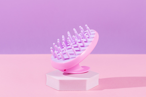 Pink scalp massage and cleansing shampoo brush on purple background, closeup. Accessories and treatment for healthy hair
