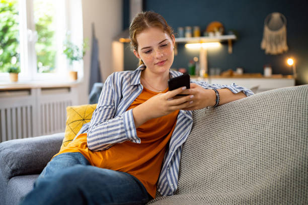 rothaariges kaukasisches teenager-mädchen mit handy, während es auf dem sofa sitzt - weiblicher teenager allein stock-fotos und bilder