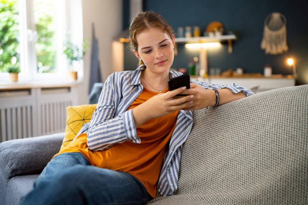 Redhead Caucasian teenage girl, using mobile phone, while sitting on the sofa in the living room