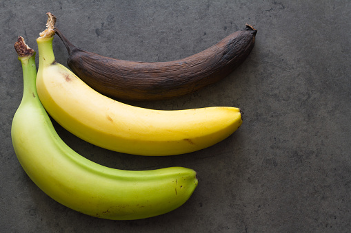 Green, yellow and brown banana on dark background, three level of ripeness of bananas, concept idea
