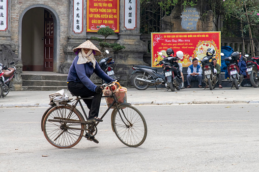 Bac Ha, Vietnam-April 2023; Woman on a bicycle in front of the temple and basket on the handlebars on her way to the Bac Ha Sunday market where mostly meet to trade and socialize