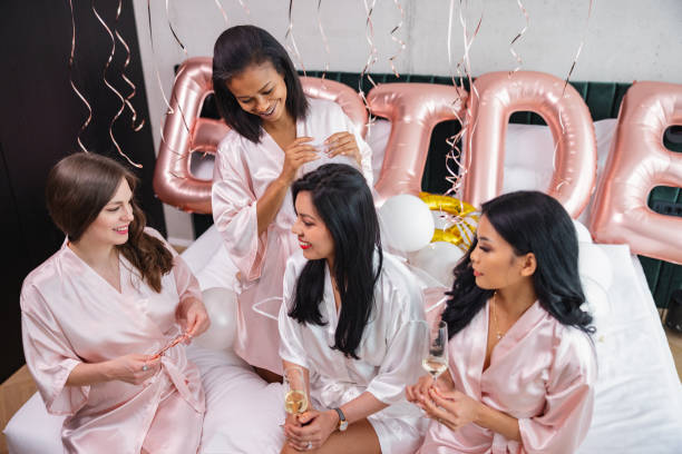 un groupe de meilleures amies féminines diverses mettant un bandeau de « mariée » sur la tête de la future mariée lors d’un enterrement de vie de jeune fille - wedding black and white weddings rose photos et images de collection