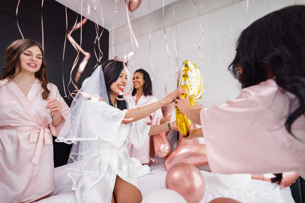 Happy Bride-To-Be And Her Bridesmaids Playing With Balloons At A Bachelorette Party A Latin bride-to-be and her diverse friends having fun and smiling while playing with the balloon decorations in the bedroom. They are jumping on the bed and having fun. Fun bachelorette activities. bachelorette party stock pictures, royalty-free photos & images