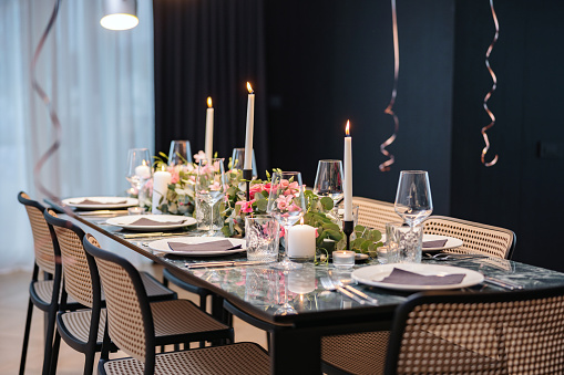 Side view of an amazing dinner table. The blue marble table is decorated with beautiful pink flowers and white candles. The plates are covered with napkins.