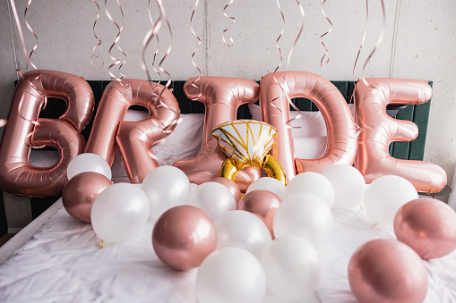 Beautiful pink balloons on a hotel bed before a bachelorette party. The balloons are spelling the word 'bride'. The room is illuminated by the natural light from the windows.