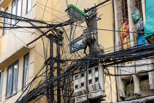 Low angle view of the façade of typical houses in Hanoi, Vietnam with electricity cables, telephone lines hanging in disarray and chaotically against the wall