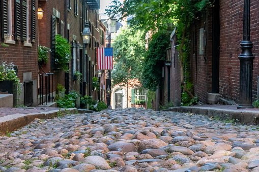 Boston, MA, USA-August 2022; Frog’s eye view down the cobblestones of Acorn Street that is lined with former coachmen homes in the Beacon Hill neighborhood; background out of focus