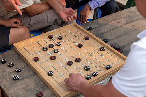 High angle view of the board of Xiangqi game, also called Chinese chess or elephant chess with hands of players and observers around board on the Sunday Market in Bac Ha, Vietnam