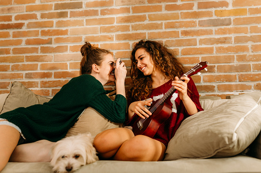 Cheerful girls bonding and having fun in the living room taking photos with digital camera