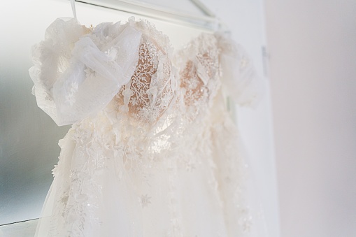 A wedding white dress hung on the wall beside a mirror