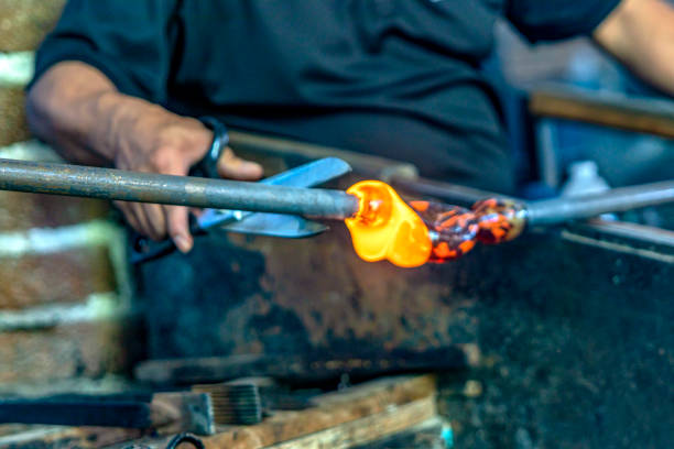 istock Old craftsman with scissors cutting and blowing the glass in fusing temperature to make a bottle with the old technique of blown glass, it is a very old and craft technique. 1502889320