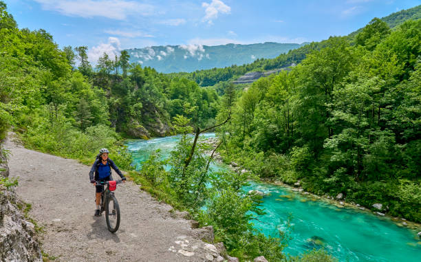 woman cyling at river Soca in Slovenia nice senior woman on a bike tour along  River Soca with her electric mountain bike  in the Triglav National Park in Slovenia soca valley stock pictures, royalty-free photos & images