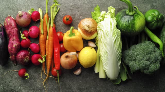 Stop motion clip of various rainbow graduated colorful fresh vegetables moving across the screen.