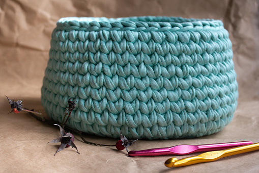 Basket made of cotton cord on a background of light brown wrapping paper and crochet hooks