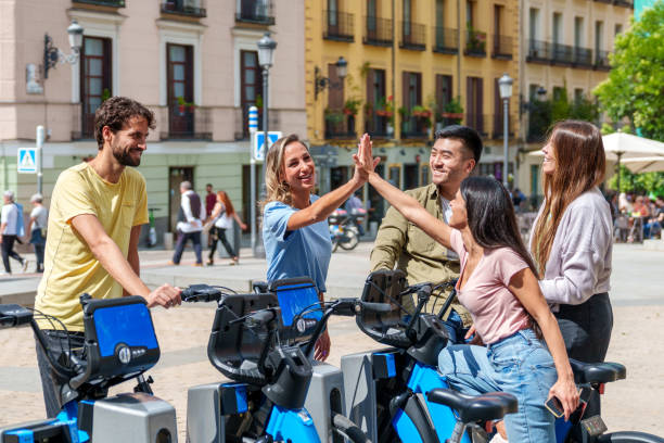 alegres amigos multiétnicos alquilando bicicletas eléctricas en un día soleado en la ciudad - metropolis building fotografías e imágenes de stock