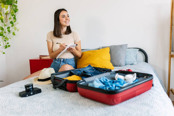 Young beautiful woman sitting on bed packing her suitcase for travel vacation stock photo