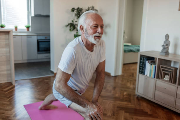 istock Caucasian senior man doing stretching exercise while sitting on yoga mat at home. Attractive mature man training indoors working out legs. 1502899986