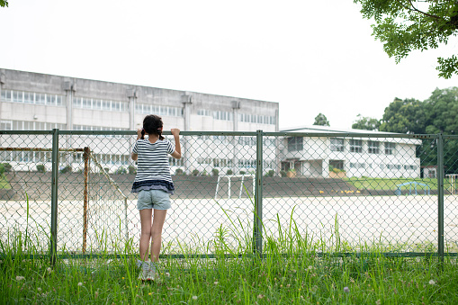 Child looking at school from outside the fence