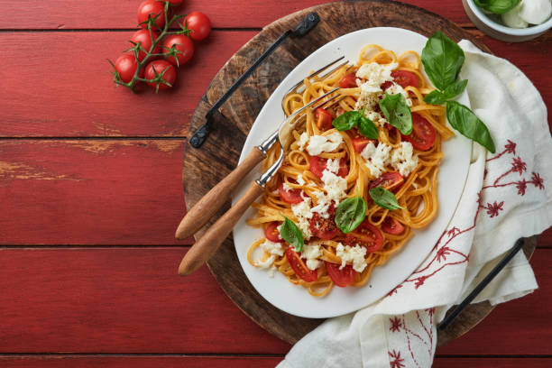 salat-caprese oder pasta-spaghetti gebrochen mit basilikum und mozzarella ala caprese auf einem weißen teller auf rotem rustikalem holzhintergrund. traditionelle italienische küche. italienisches food-konzept.  draufsicht. - caprese salad antipasto wine mozzarella stock-fotos und bilder