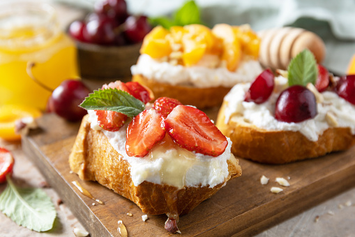 Berries toast breakfast, healthy food. Sandwich with cherry, strawberries, soft cheese and honey on wooden board on a stone  background.