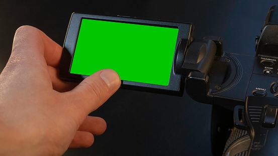 A Caucasian male using a flip screen of a video recording camera with a green screen