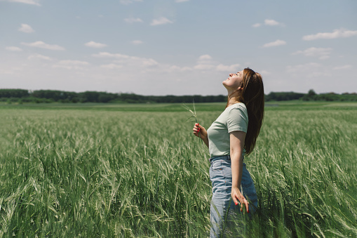 A woman enjoys the fresh air in nature in a green barley field. Summer countryside and gathering flowers. Atmospheric tranquil moment