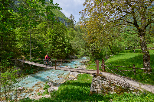 woman crossing  River Soca with her electric mountain bike over a suspension bridge in the Triglav National Park in Slovenia