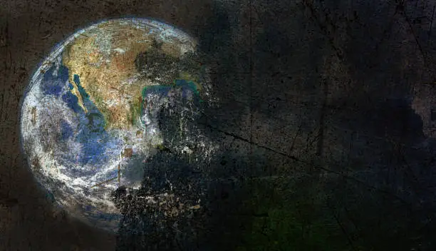 View of an image of the world peeling off a moody dark background of scratched and discolored concrete. Illustrate global problems, climate change, extinction, economic problems, etc.