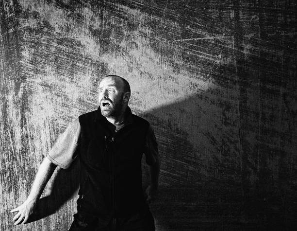 Frightened man up against a scratched grungy concrete wall, horrified and with his mouth and eyes open wide.