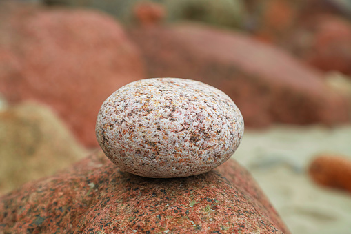 A pastel pink round small stone balanced on big red granite rock. Photo with selective focus