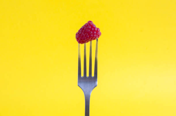 Raspberry stabbed on a silver fork on the yellow background. Close-up.