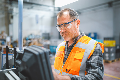 Professional mid-adult industrial factory male employee concentrated, working, putting, checking, and testing with a product line of industrial equipment cables manufacturing plant in a large electronics factory warehouse