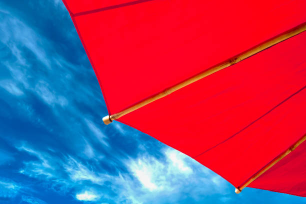 istock Red Beach Umbrella on the Beach. Umbrella Isolated on Blue Sky Background with Clouds 1502932694