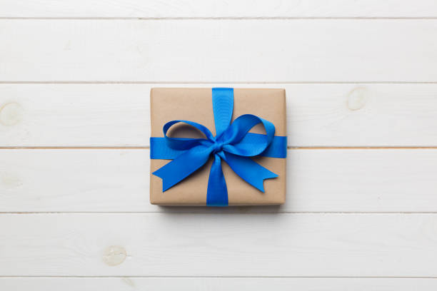 istock Holiday gift box wrapped in craft paper with colored bow on table background. Top view, flat lay, copy space 1502932898