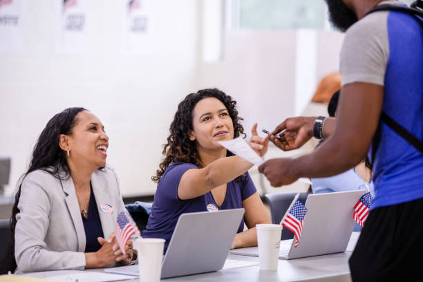 Cheerful female volunteers help unrecognizable man with ballot stock photo