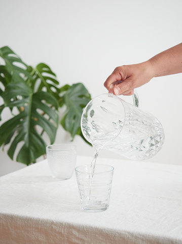 Drink water, healthy lifestyle. Concept of thirst and hydration. Woman's hand pouring fresh and pure water from a pitcher into a glass at the table.