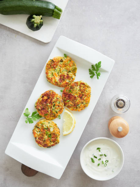 istock zucchini fritters or cutlets . Served in white rectangular plate with fresh parsley and lemon, on the table yogurt sauce as dressing, salt and pepper shakers. 1502937634