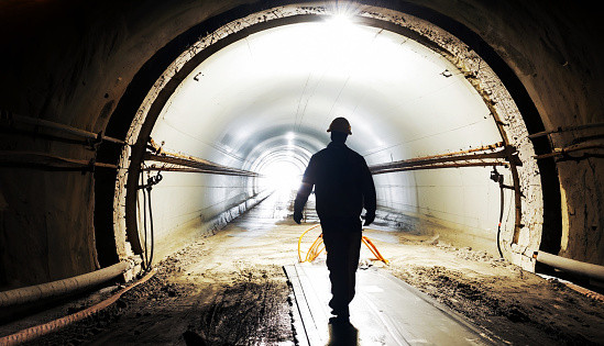 Underground tunnel construction with silhouette of walking worker. The way to the light at the end of the tunnel.