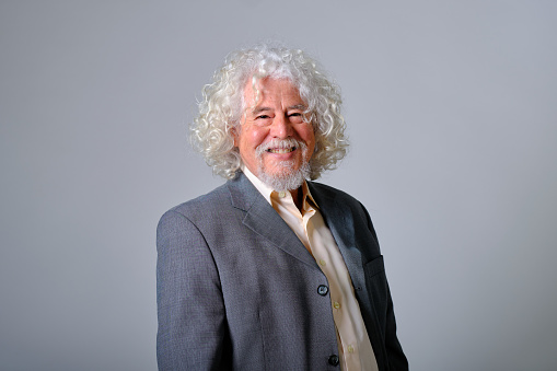 front view portrait of a caucasian old man with white and wavy hair in a gray background studio