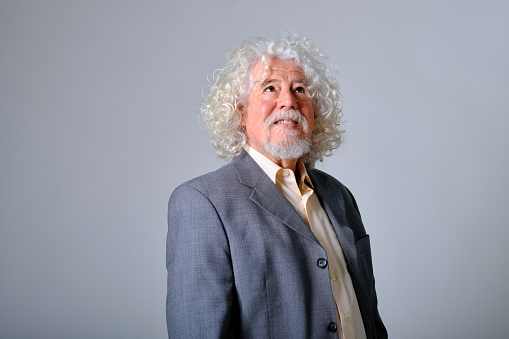 front view portrait of a caucasian old man with white and wavy hair in a gray background studio