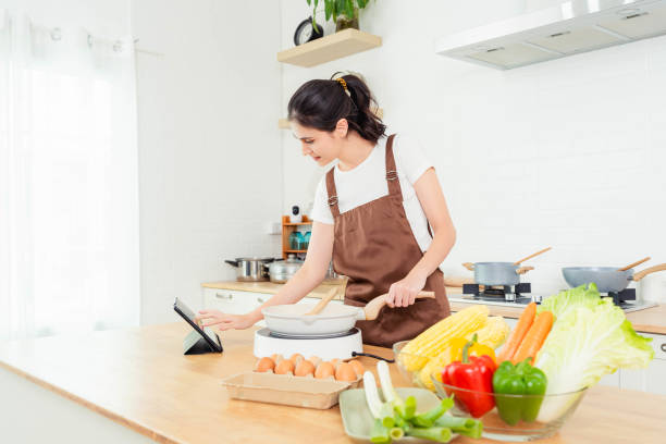 istock Young beautiful woman learning online cooking class digital tablet computer in kitchen at home Young lady learns to cook by watching video recipes on tablet in kitchen She learn cooking by herself 1502943319