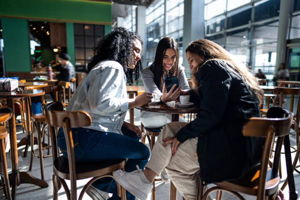 amigos usando el teléfono en la cafetería del aeropuerto - mobile phone coffee shop group of people women fotografías e imágenes de stock