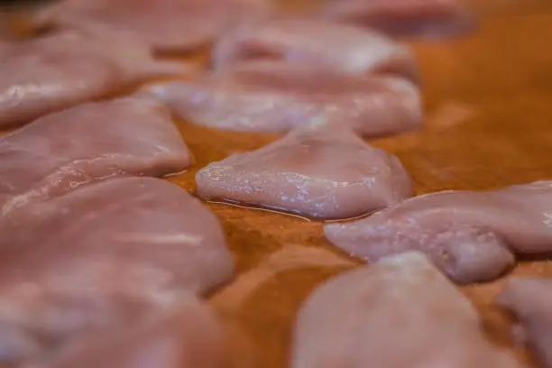 Photo of Slices of natural organic chicken schnitzel on a wooden cutting board ready for seasoning. Fresh meat. Protein replenishment