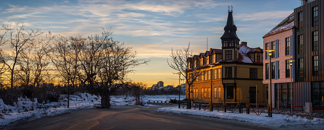 Facade of typical Reykjavik houses illuminated by the last rays of the evening sun reflecting orange and gold light with snowy sidewalks and a subtly cloudy sky with twilight tones