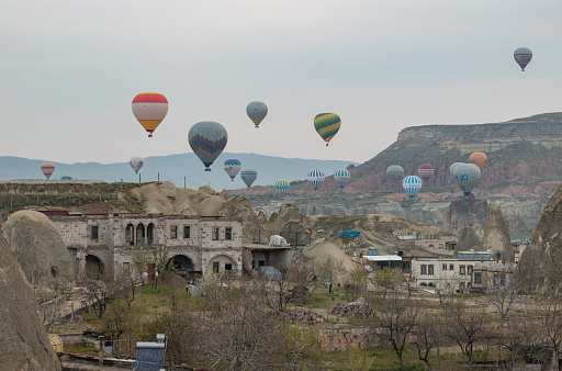 Goreme, Turkey - April 12, 2023: A picture of hot air balloons flying over the Goreme Historical National Park and the town of Goreme at sunrise.