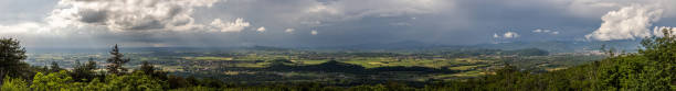 panoramic composition with 180 degrees view of the beautiful hilly territory in the eastern area of the Friuli Venezia Giulia region, in Italy, in the afternoon, partially illuminated by the sunlight, under a huge stormy cloud composición panorámica con vista de 180 grados del hermoso territorio montañoso en la zona oriental de la región de friuli venezia giulia, en italia, por la tarde, parcialmente iluminado por la luz del sol, bajo una enorme nube tormentosa