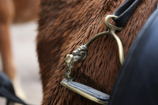 Side close up on the metal foot stirrup on a black leather horse saddle