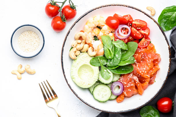 istock Keto salad with spinach, salmon, shrimp, avocado, cucumber, tomato, nuts, sesame seeds. Low-carbohydrate lunch rich in healthy fats. White table background, top view 1502962425